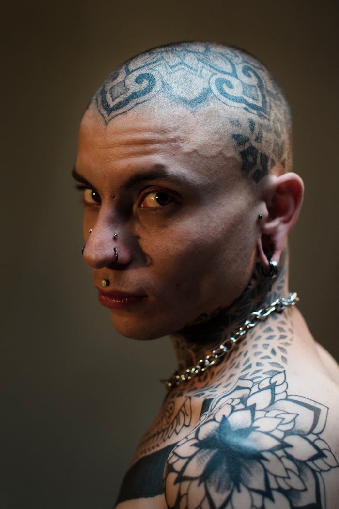 our-story-01 Artistic portrait of a tattooed individual pierced, showcasing intricate body and face art.
