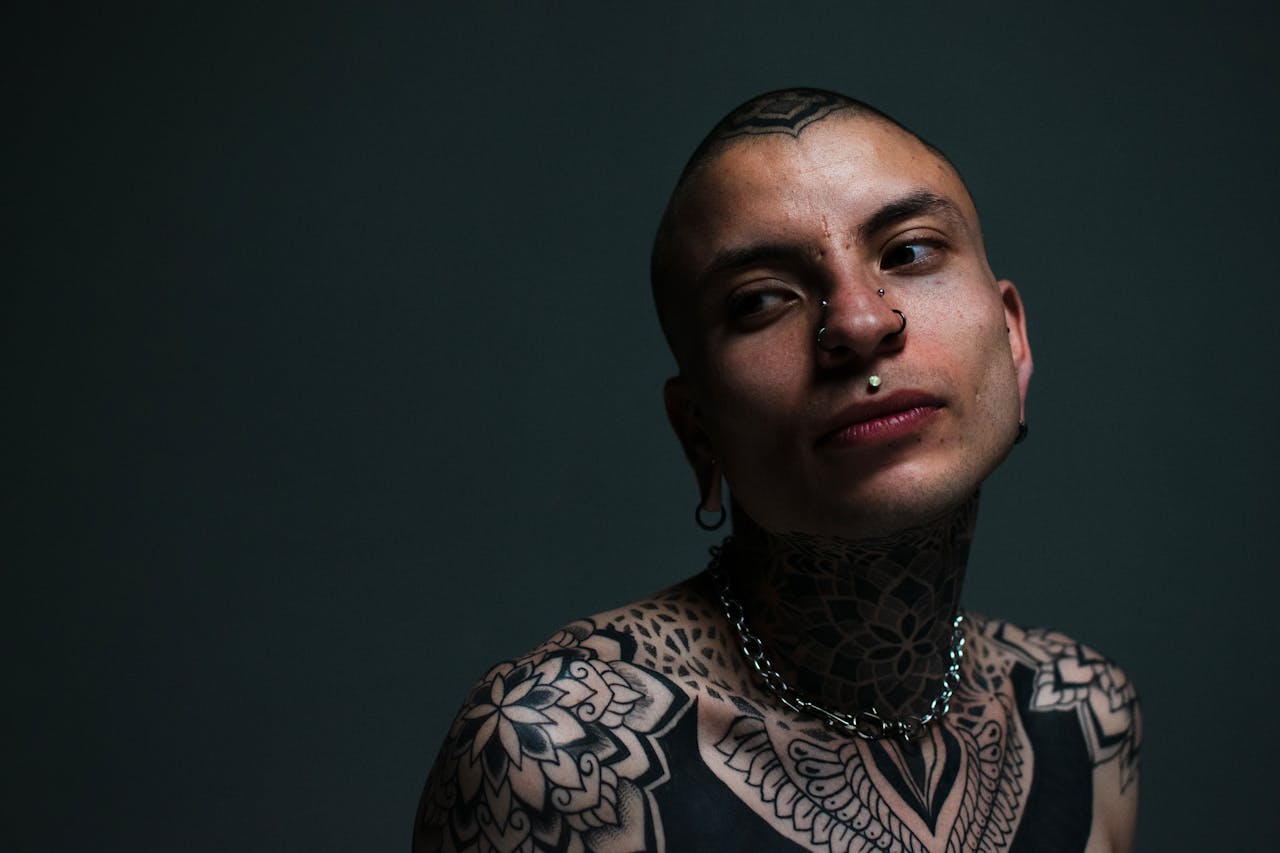 Close-up portrait of a tattooed person with facial piercings and bold body art.