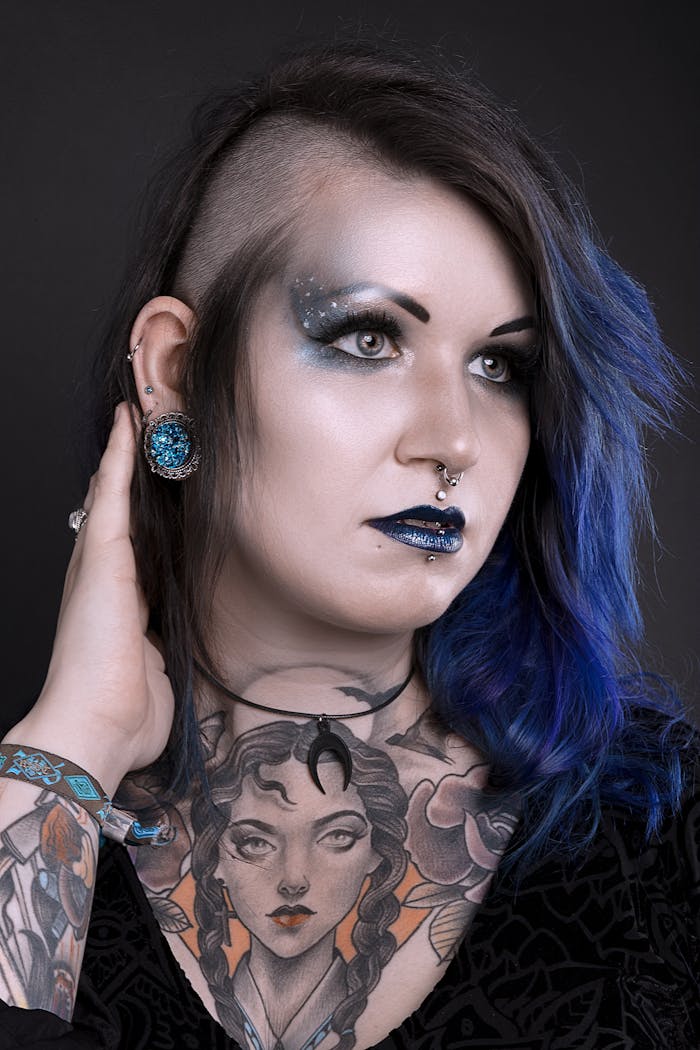 Artistic portrait of a woman with tattoos and bold cosmic-themed makeup in a studio setting.